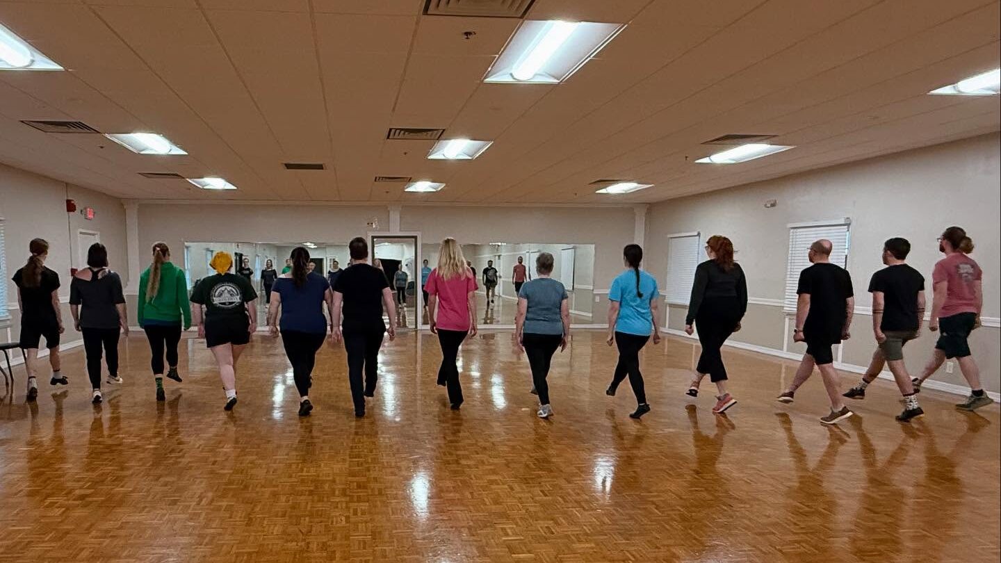 Dancers in a line moving away from the camera towards a mirror.